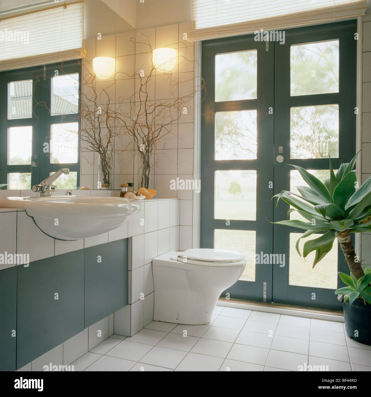 Lumière murale sur le mur à côté de double portes modernes de salle de bains avec carrelage blanc équipée lavabo et toilettes sur sol carrelé coiffeuse Banque D'Images