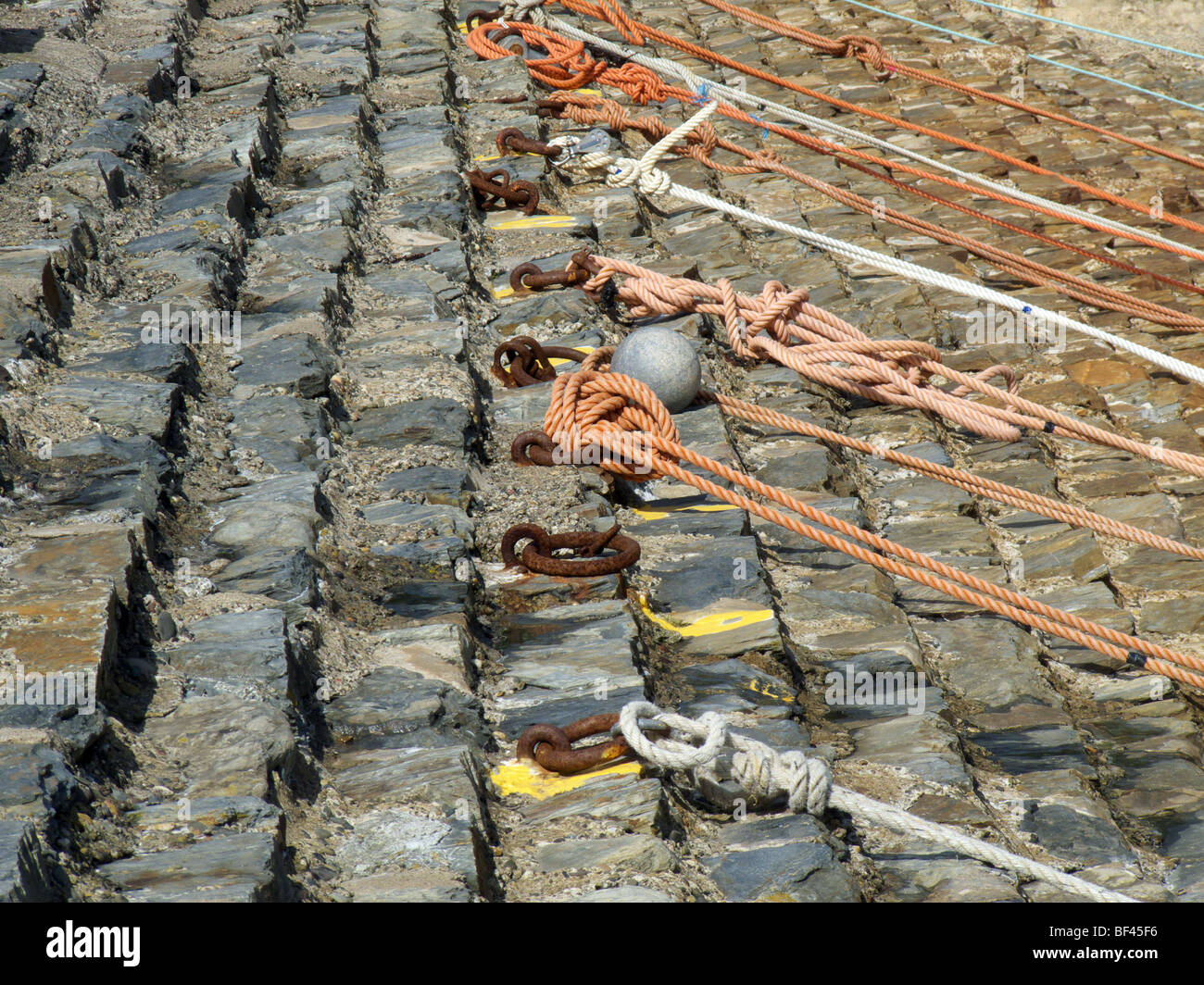 Ancienne en pierre grise épaulement galets mur du port avec rusty anneaux d'amarrage et cordes Banque D'Images