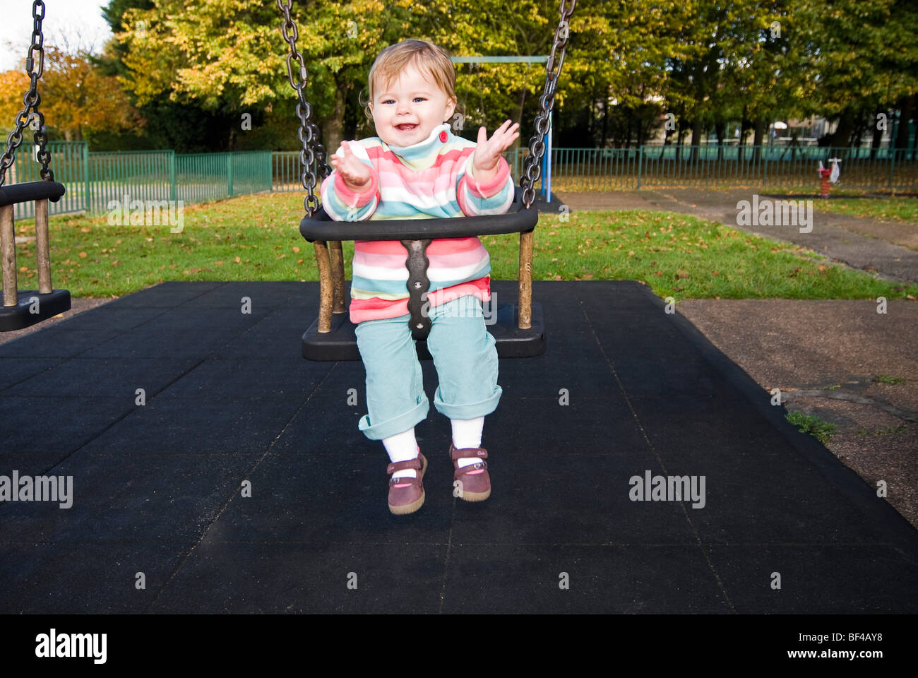 Close up portrait of horizontal d'une petite fille de sourire et de clapping assis sur une balançoire dans un parc au soleil. Banque D'Images