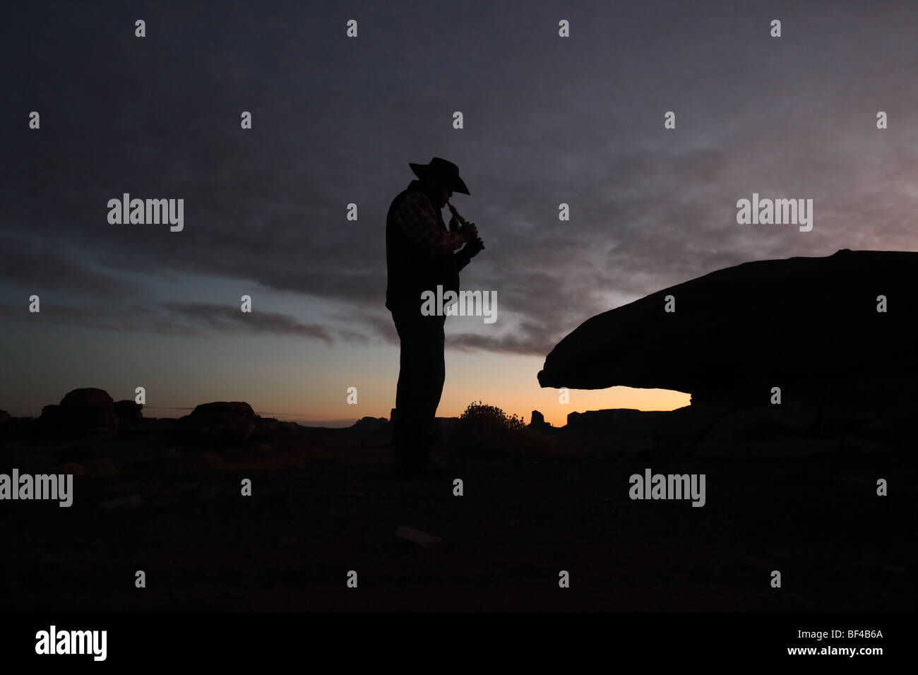 Homme Navajo à l'instrument traditionnel en silhouette au lever du soleil dans la Vallée de Monument Banque D'Images