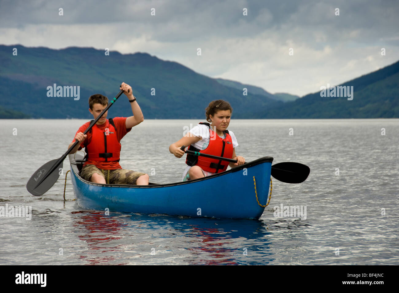 Un jeune homme et une jeune femme caucasien portant des gilets de sauvetage rouges pagayant un canot canadien bleu sur le Loch Earn, dans le Perthshire, en Écosse. ROYAUME-UNI Banque D'Images
