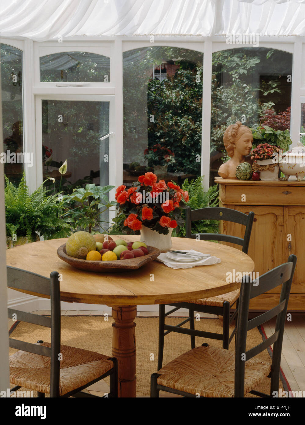 Retour à l'échelle-chaises table circulaire avec vase de fleurs rouge et coupe de fruits dans la salle à manger véranda avec stores blanc Banque D'Images