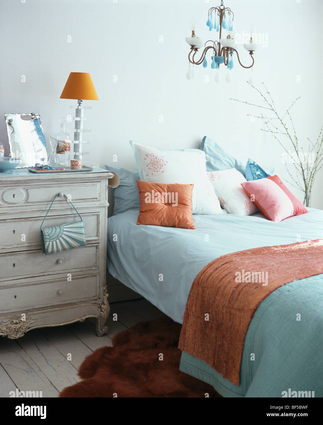 Lampe orange sur la poitrine crème-de-tiroirs à côté de lit avec draps  turquoise et orange et jeter coussin dans une chambre moderne Photo Stock -  Alamy