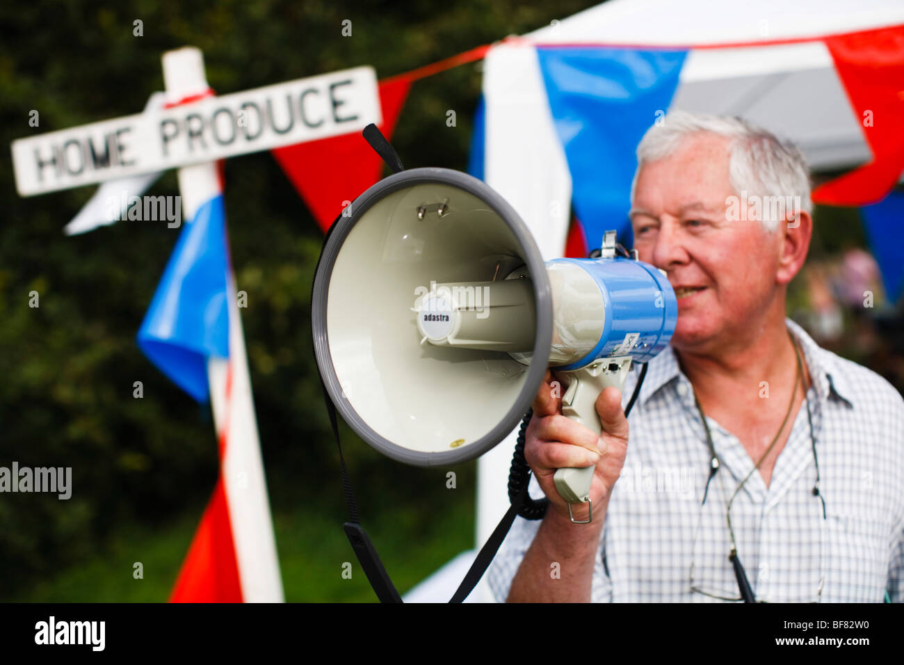 Faire de l'homme annonce sur un mégaphone lors d'une fête du village rural dans les Cotswolds, Eastleach Turville, Gloucestershire, Royaume-Uni Banque D'Images