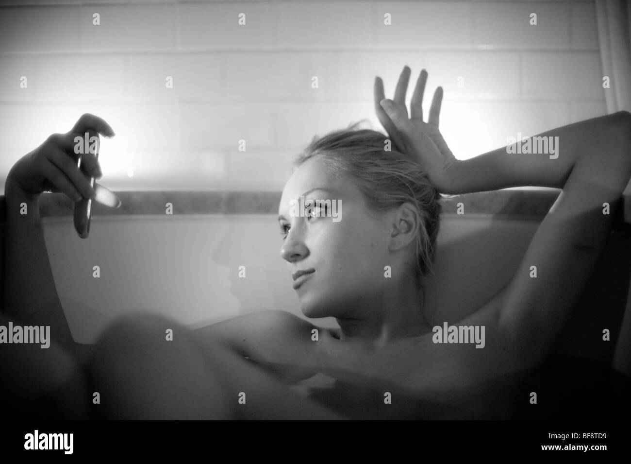 Femme à l'aide d'iPhone dans la baignoire par la lumière de bougie Banque D'Images