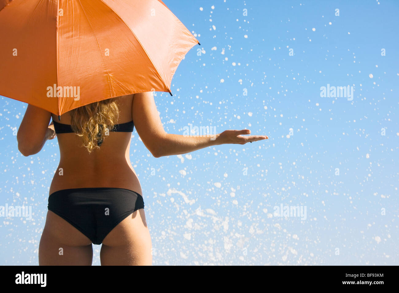 Woman holding orange umbrella against blue sky Banque D'Images