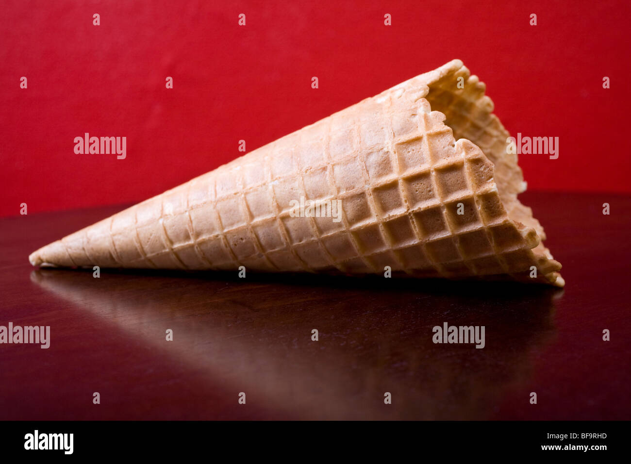Cornet de crème glacée de qualité sur une table marron contre un mur rouge. Banque D'Images
