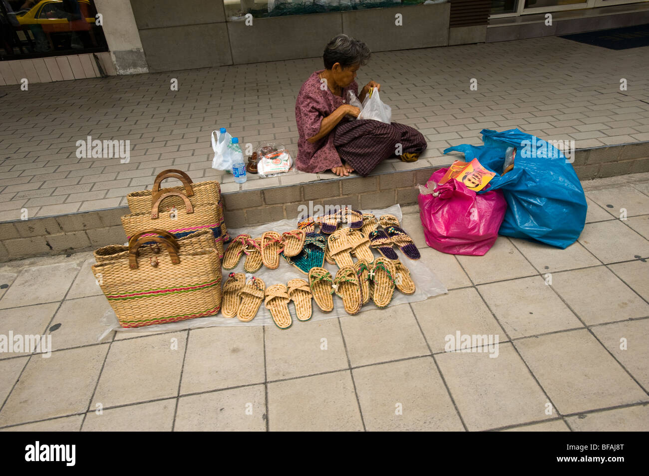 Vieille dame de vendre et de sacs à main flipflop qui a fait de l'herbe à côté de sentier, Bangkok, Thaïlande Banque D'Images