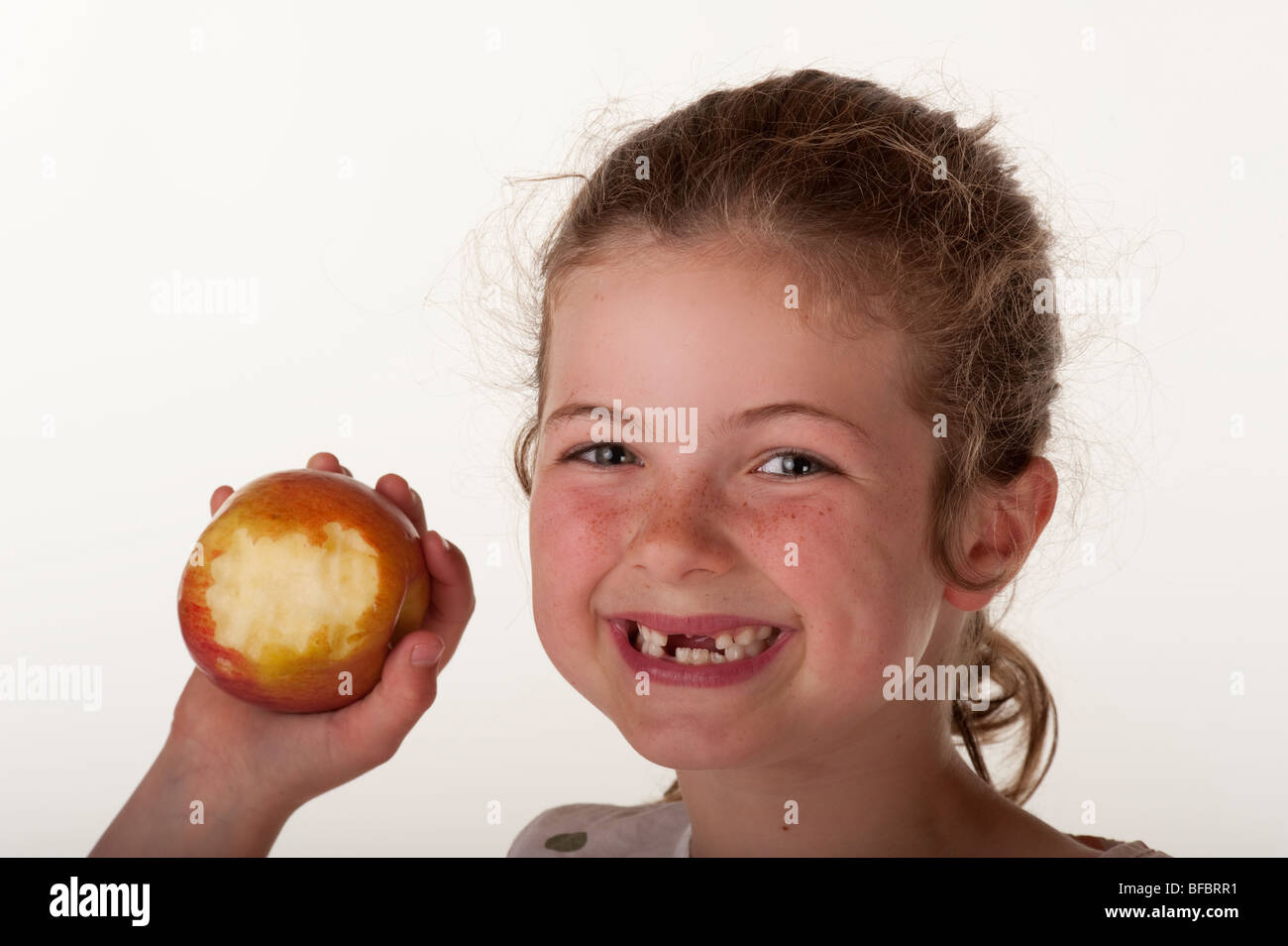 Petite fille (7 ans) qui est absente des dents avant de manger sur apple chaise de sac d'haricot rouge contre fond blanc Banque D'Images