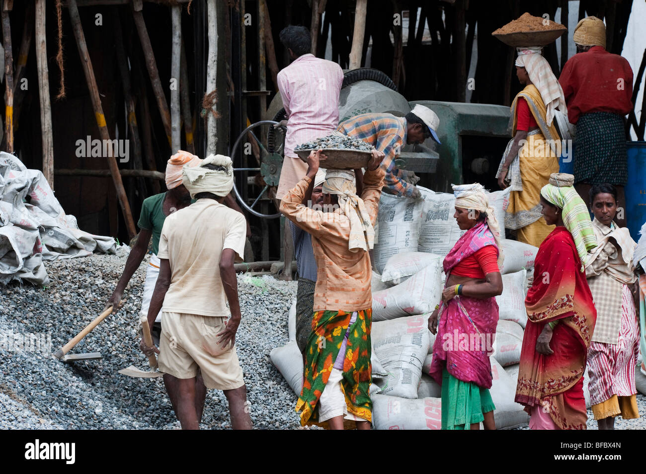 Les femmes indiennes qui travaillent sur un chantier, exerçant son activité sous le sable et la pierre sur la tête, de mettre dans une bétonnière. Puttaparthi, Andhra Pradesh, Inde Banque D'Images