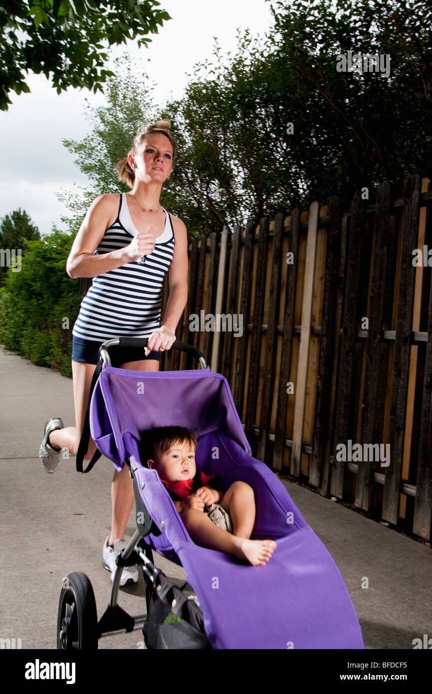 Une edgy-athlétique, à la jeune femme bénéficie d'une exécution sur un trottoir avec un bébé dans une poussette. Banque D'Images