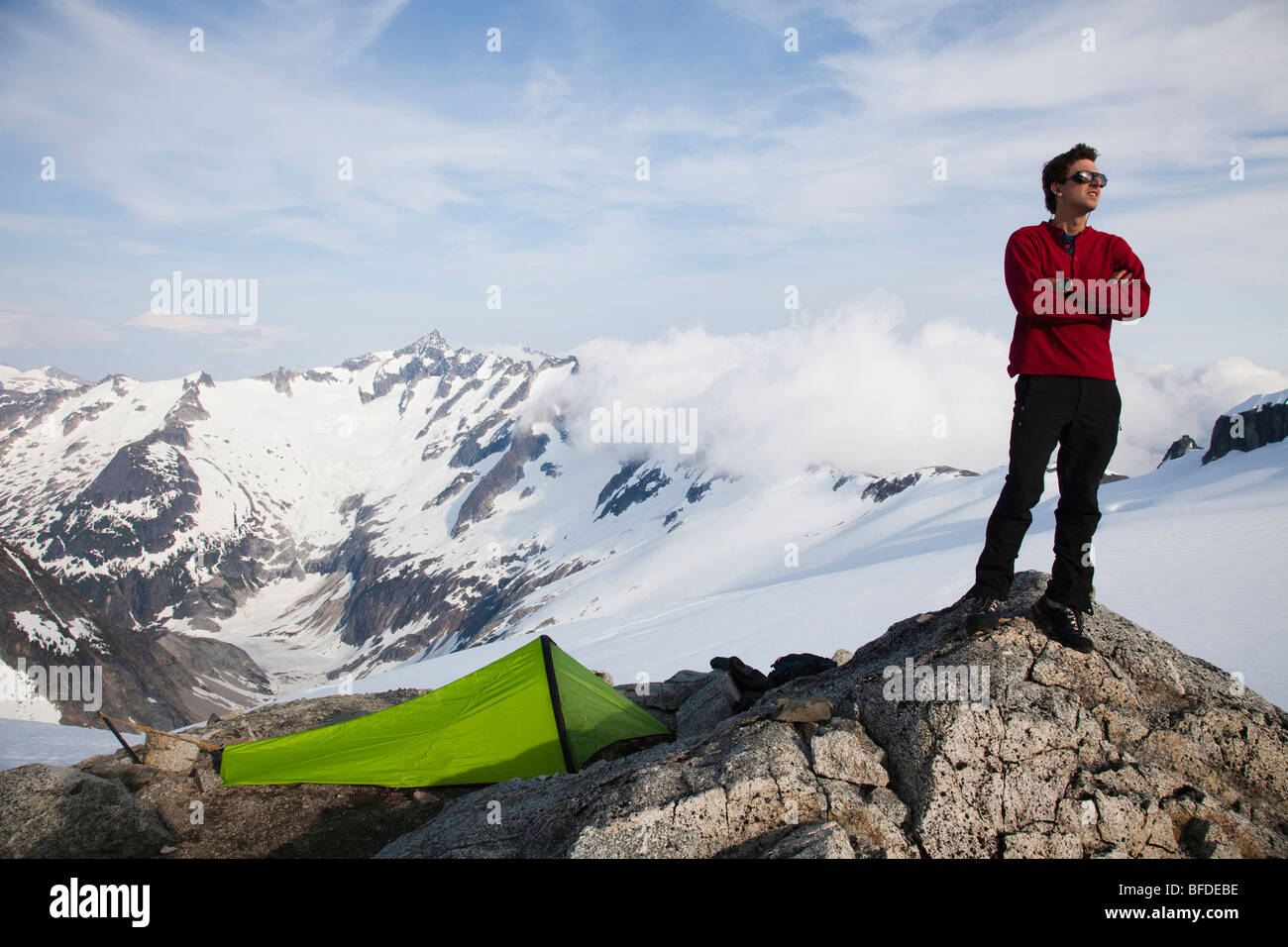 Un jeune grimpeur se dresse sur un affleurement rocheux près de sa tente pendant la montée sur un glacier dans les montagnes. Banque D'Images