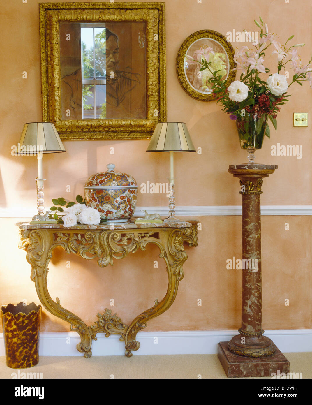 Miroir doré orné au-dessus de table console baroque en crème traditionnelle salle avec arrangement floral sur un grand socle en marbre Banque D'Images