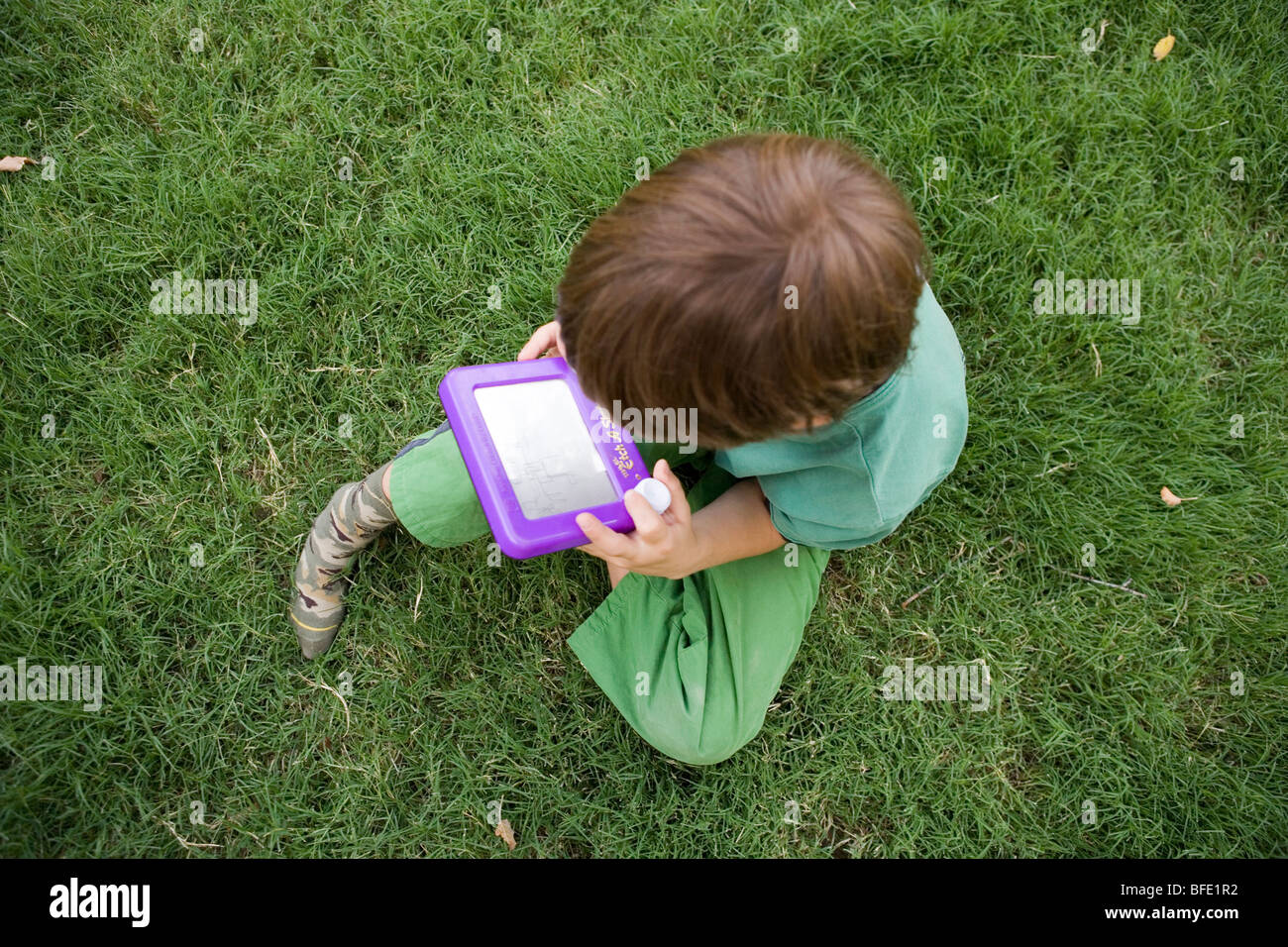 Enfant assis dans l'herbe en jouant avec d'Etch a Sketch, dessin à l'ancienne toy Banque D'Images