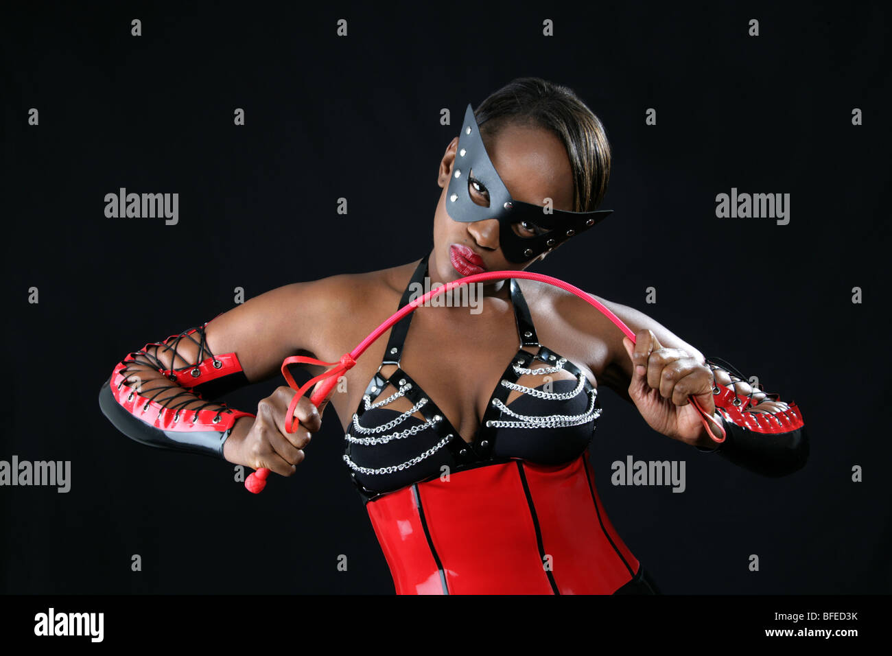 Femme portant un Africain noir et rouge Fetish Latex costume et tenant une cravache rouge. Bat Woman Fantasy Image. Banque D'Images