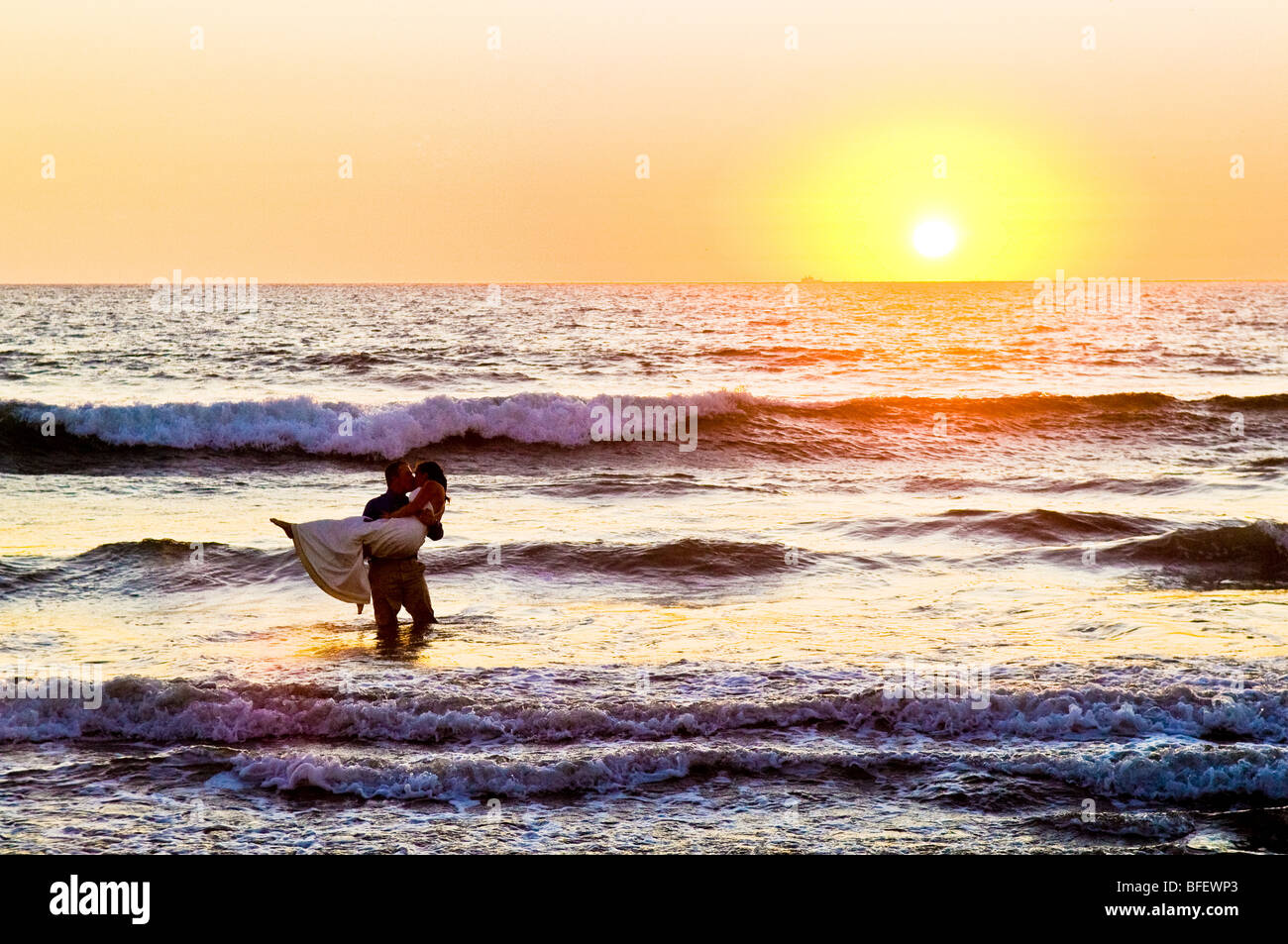 Couple dans l'océan au coucher du soleil, après leur mariage à Mazatlan, Mexique. Banque D'Images