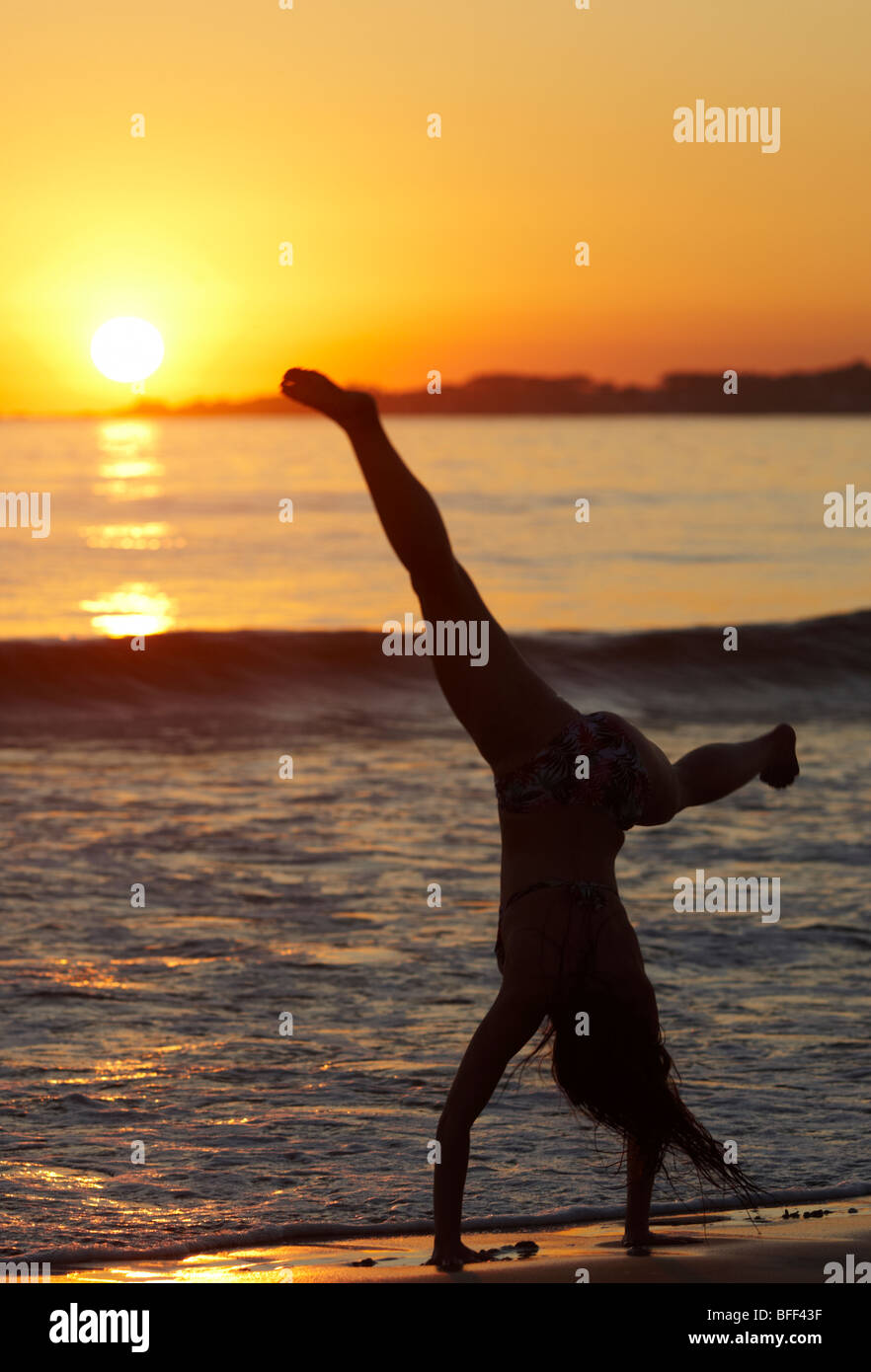 Girl roues de chariot sur la plage au coucher du soleil en silhouette Banque D'Images