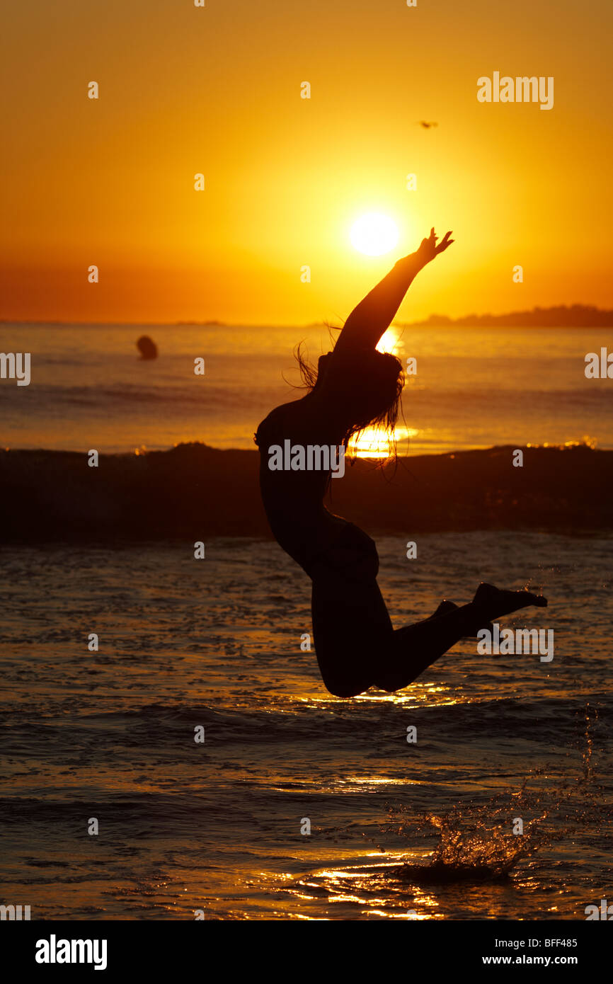 Fille silhouette saute dans la mer au coucher du soleil, Banque D'Images