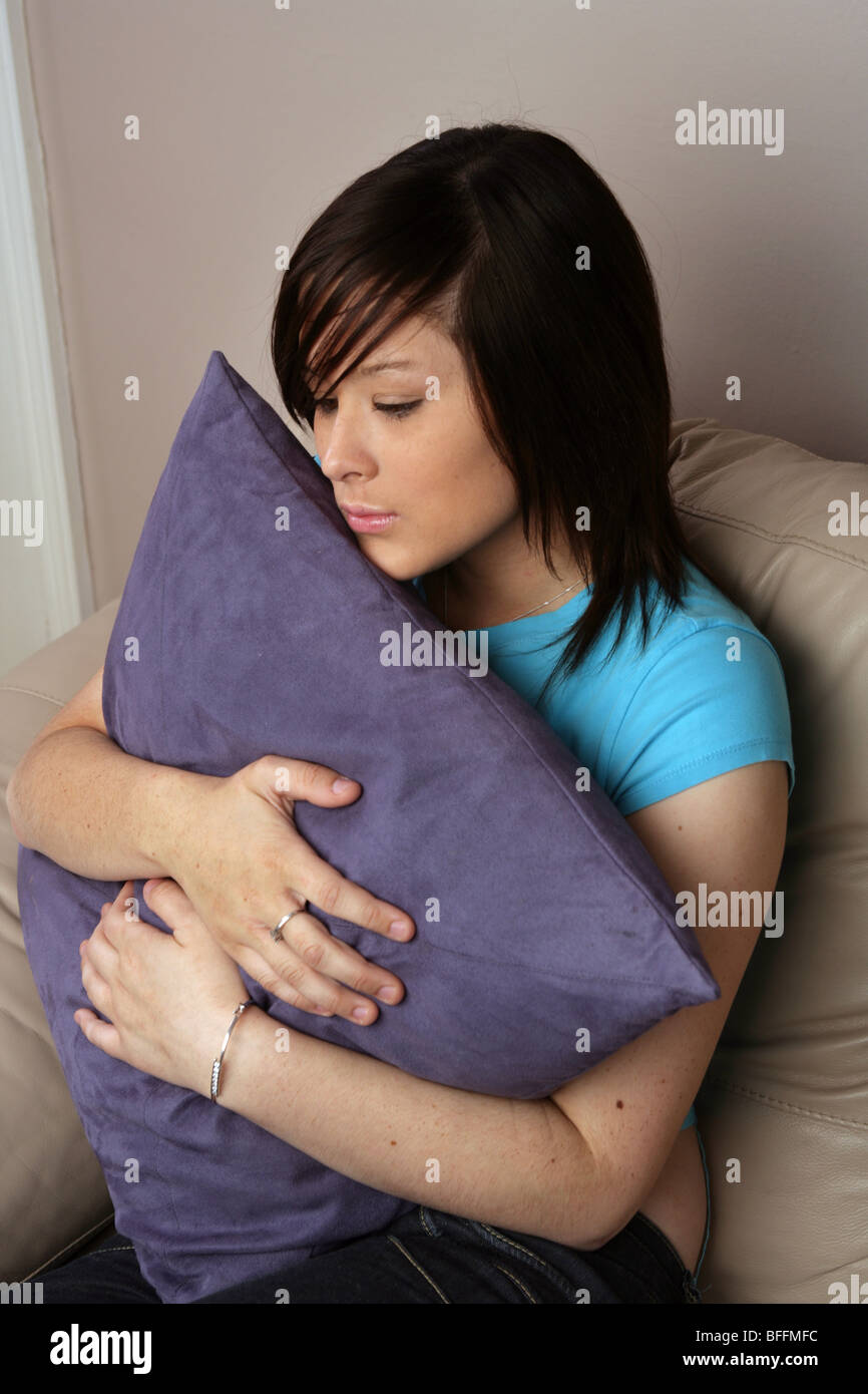 Jeune femme assise sur un grand canapé coussin hugging Banque D'Images