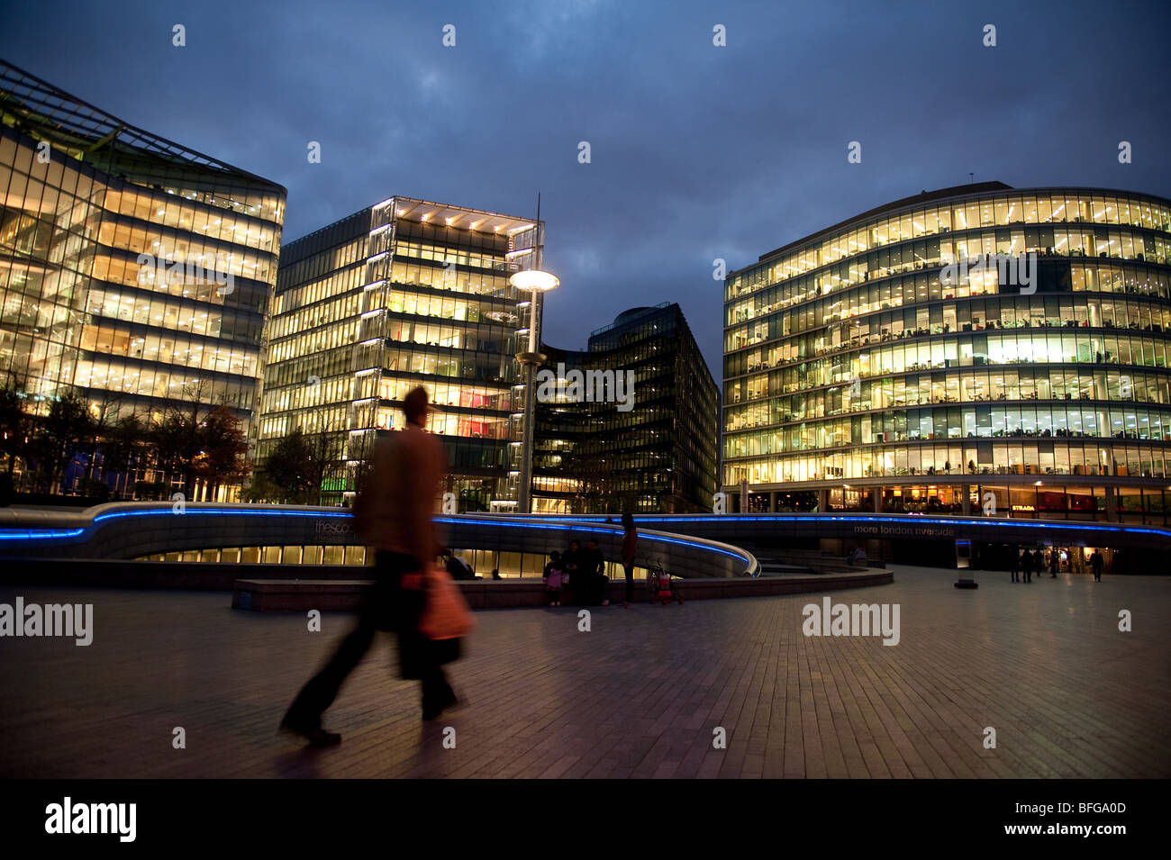 Un piéton passe par certains immeubles de bureaux par 'l'écope' sur la rive sud de la Tamise à Londres au crépuscule. Banque D'Images