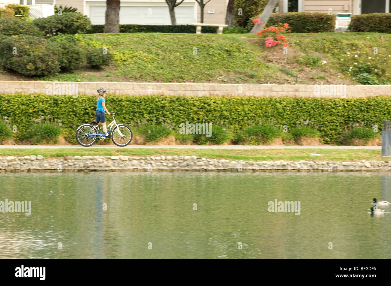 Jeune fille monte un vélo le long d'un chemin au bord du lac dans un quartier résidentiel dans la collectivité, Irvine Orange County, en Californie. Banque D'Images