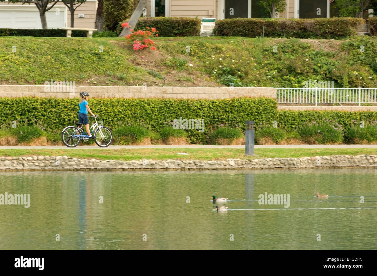 Jeune fille monte un vélo le long d'un chemin au bord du lac dans un quartier résidentiel dans la collectivité, Irvine Orange County, en Californie. Banque D'Images