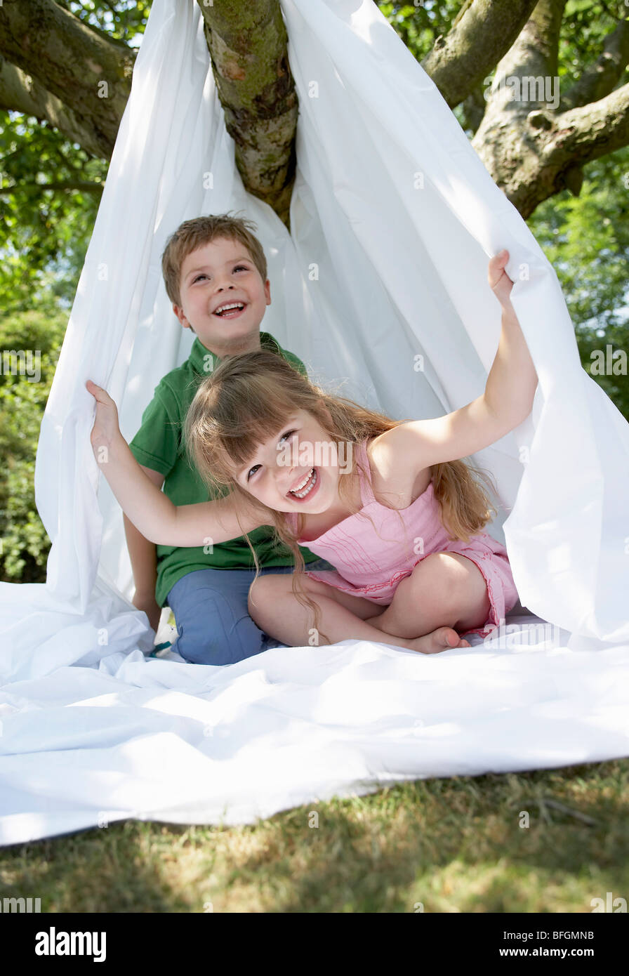Jeune garçon et fille dans la cour siégeant en tente faite de drap de lit Banque D'Images