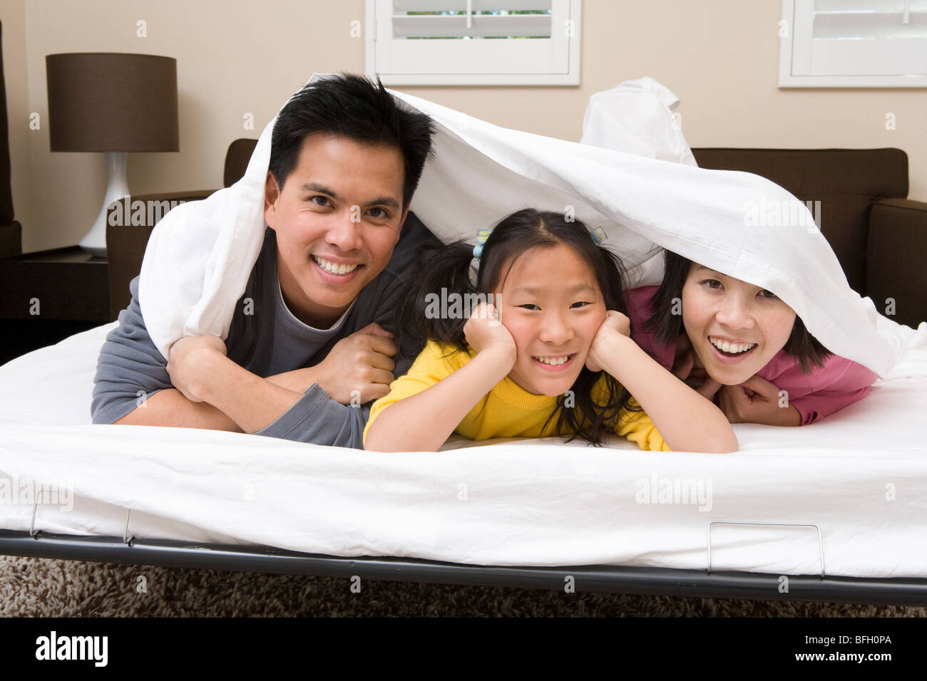 La mère, le père et sa fille couchée sur le lit recouvert de drap de lit Banque D'Images