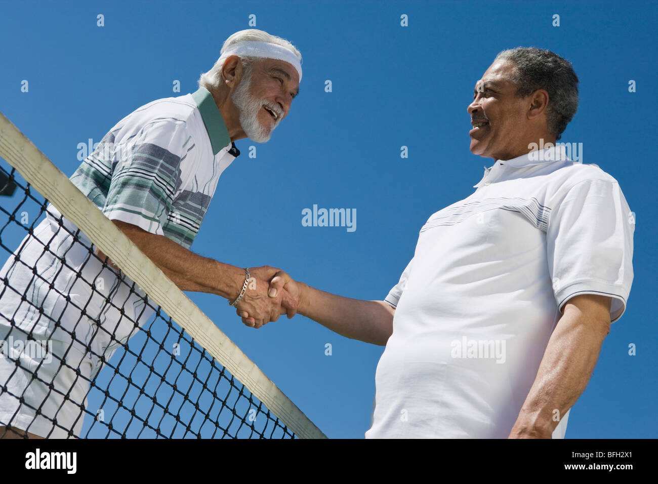 Deux hommes se serrant la main au filet de tennis Banque D'Images