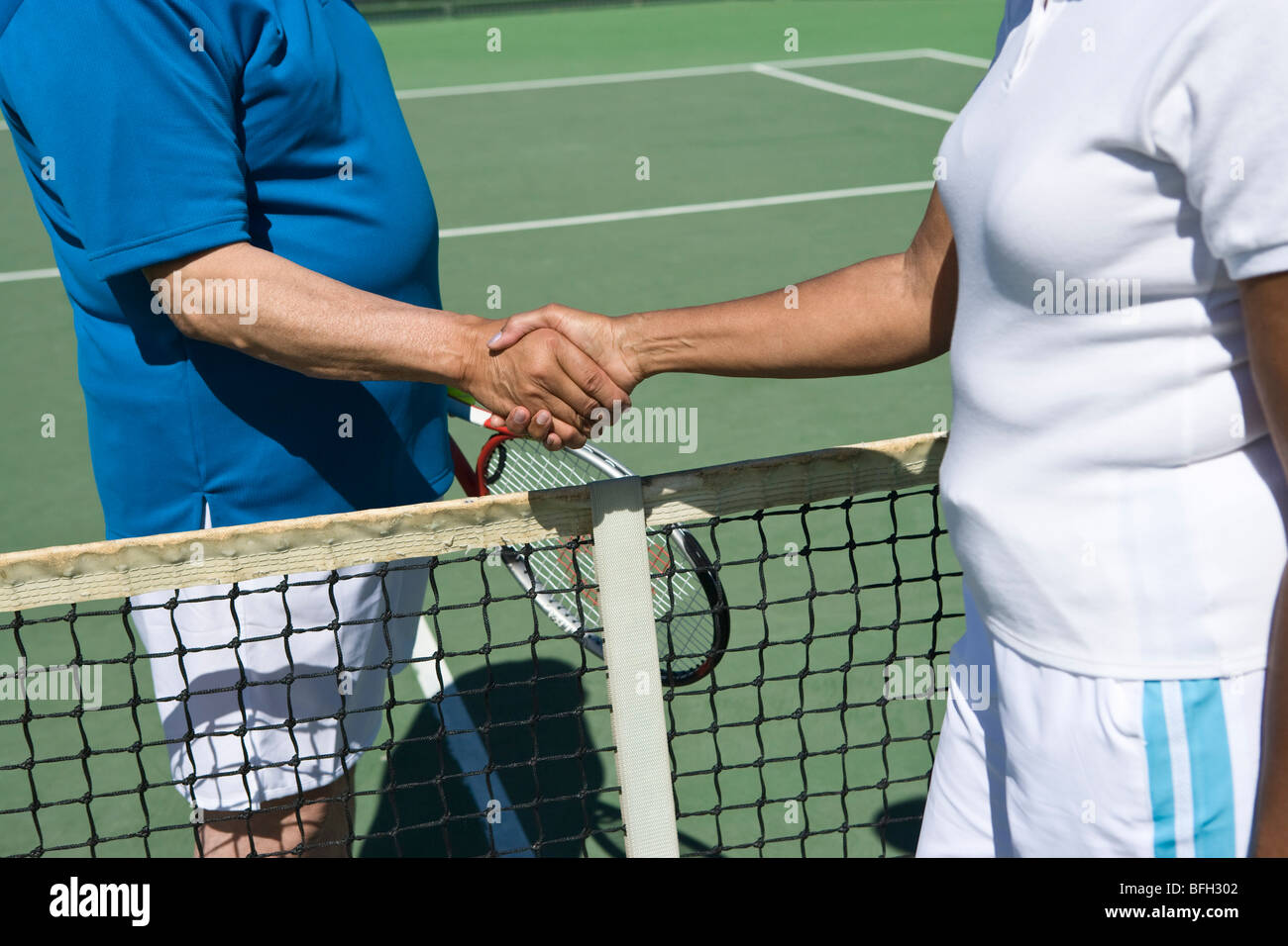 Deux personnes se serrant la main au filet de tennis Banque D'Images