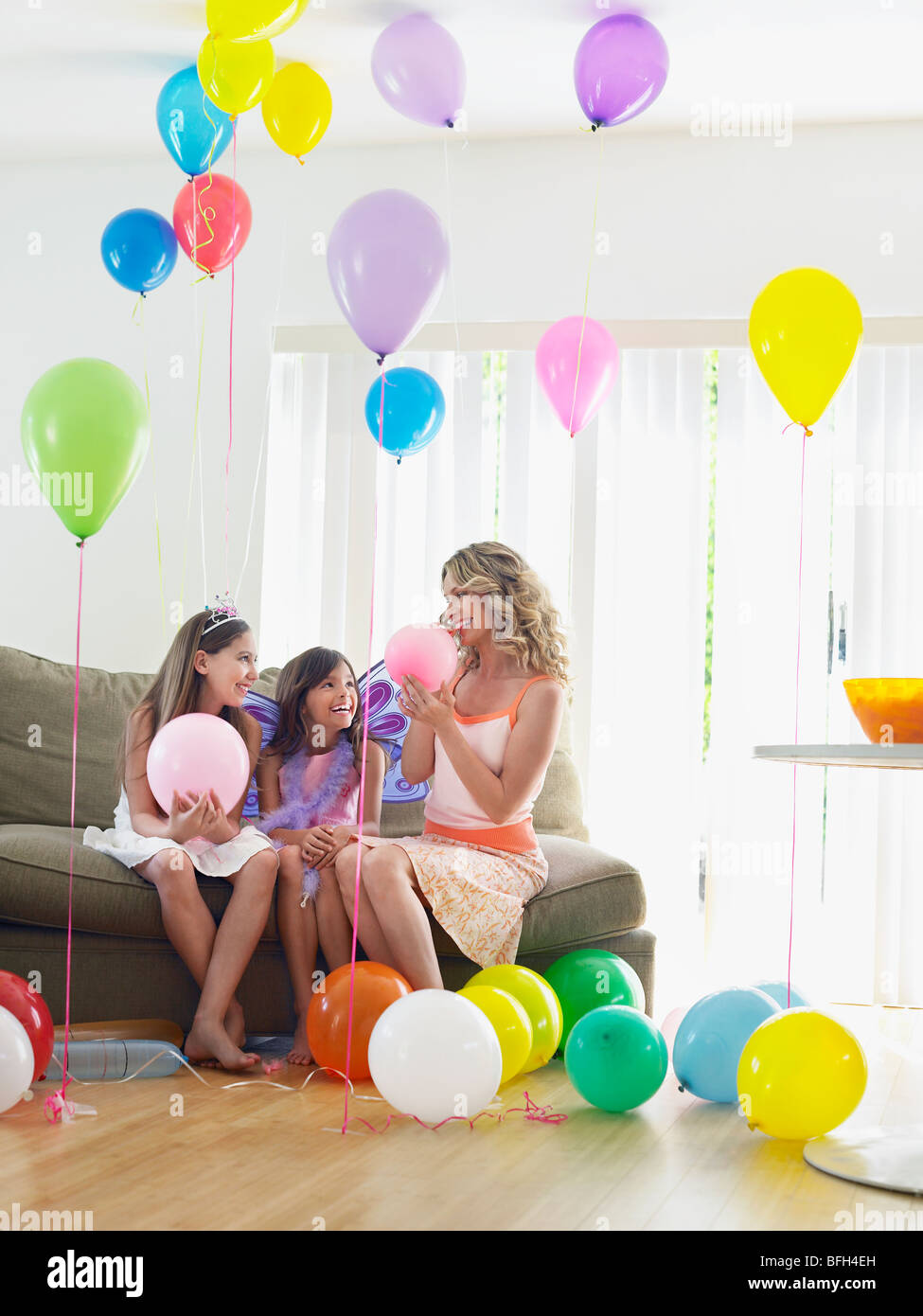 Deux jeunes filles (7-9, 10-12) avec la mère assis sur un canapé dans la salle pleine de ballons Banque D'Images
