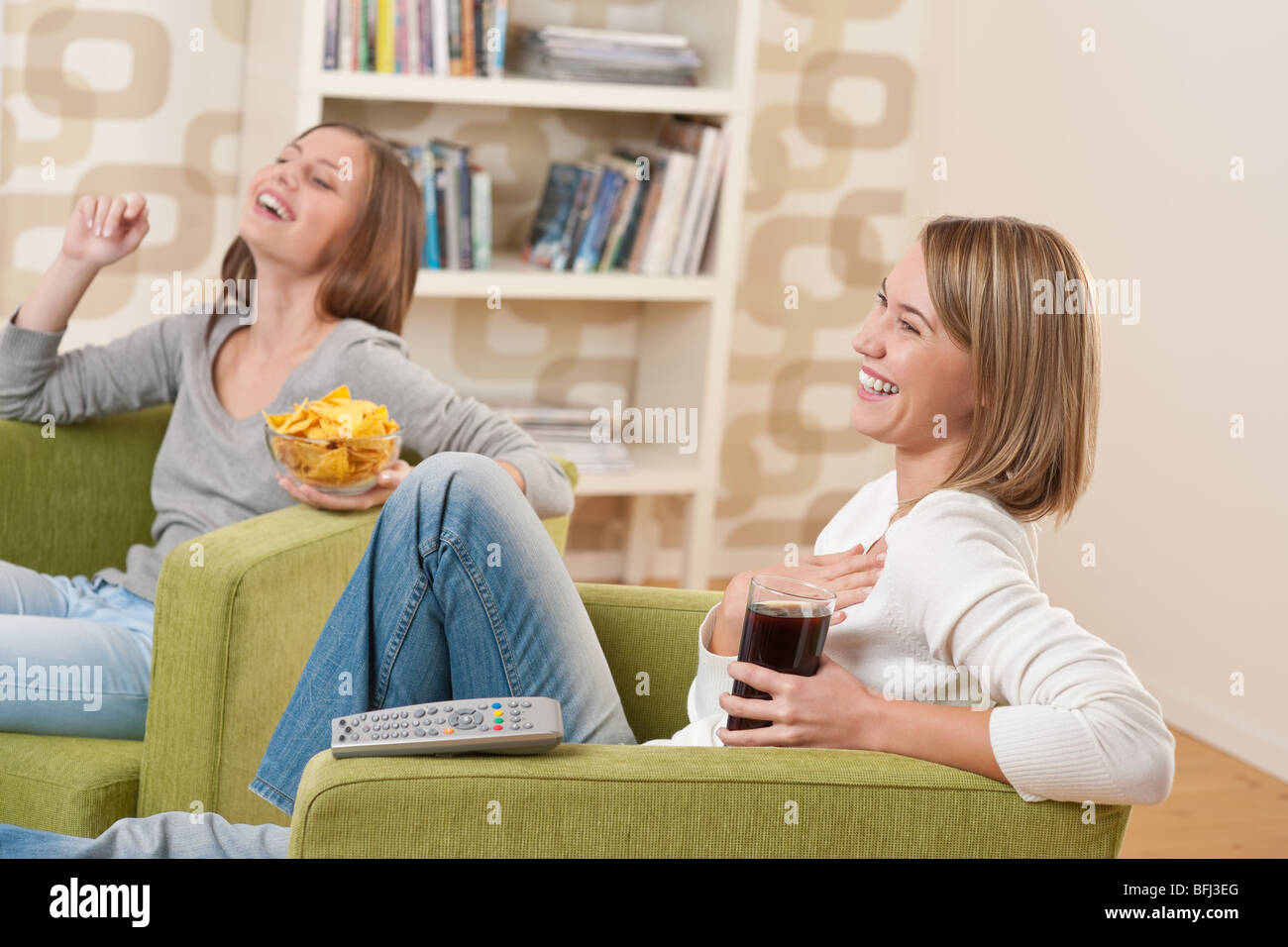 - Deux étudiants female teenager regardent la télévision ensemble, manger des chips Banque D'Images