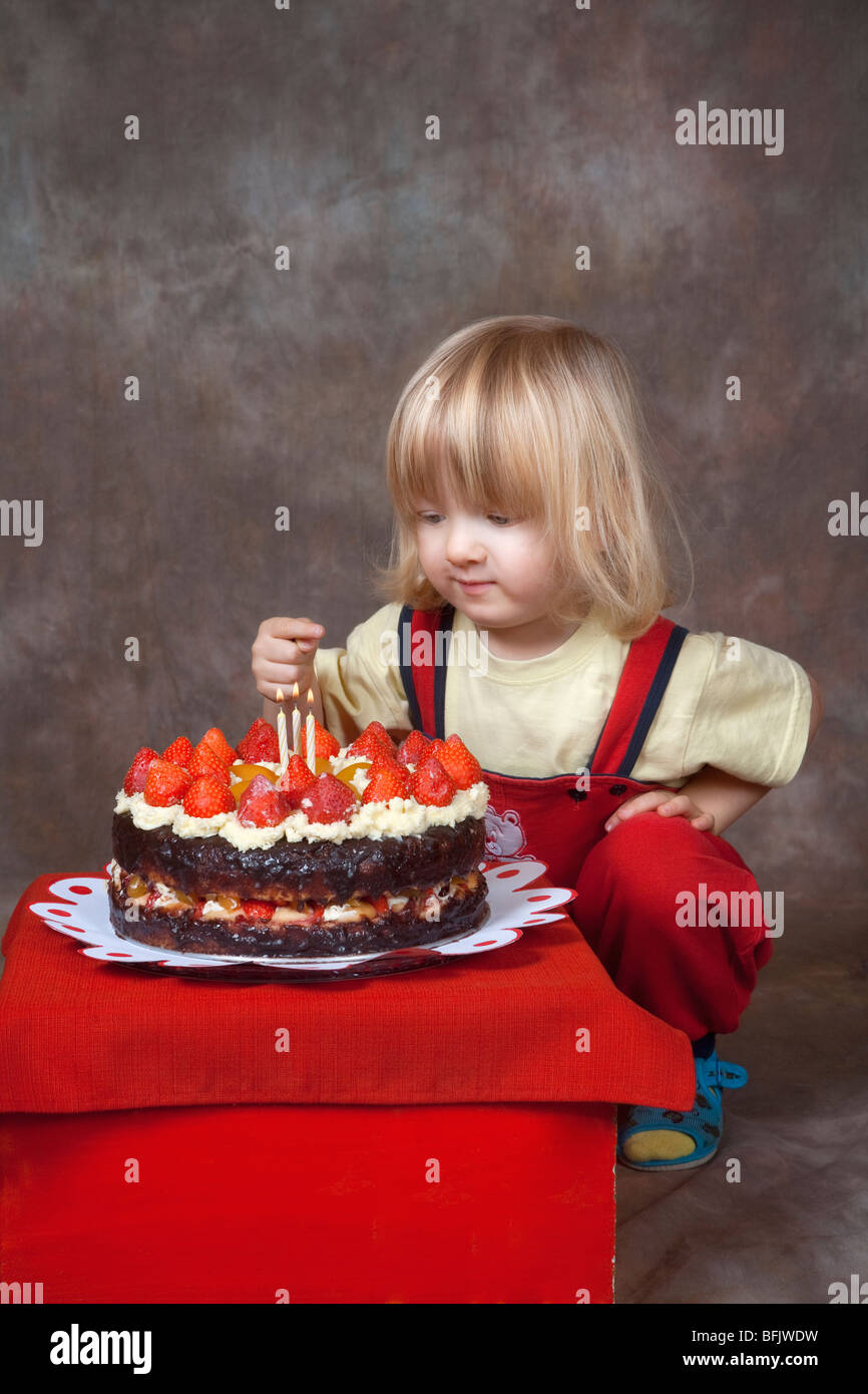 Garçon avec de longs cheveux blonds regardant les bougies sur son gâteau d'anniversaire Banque D'Images