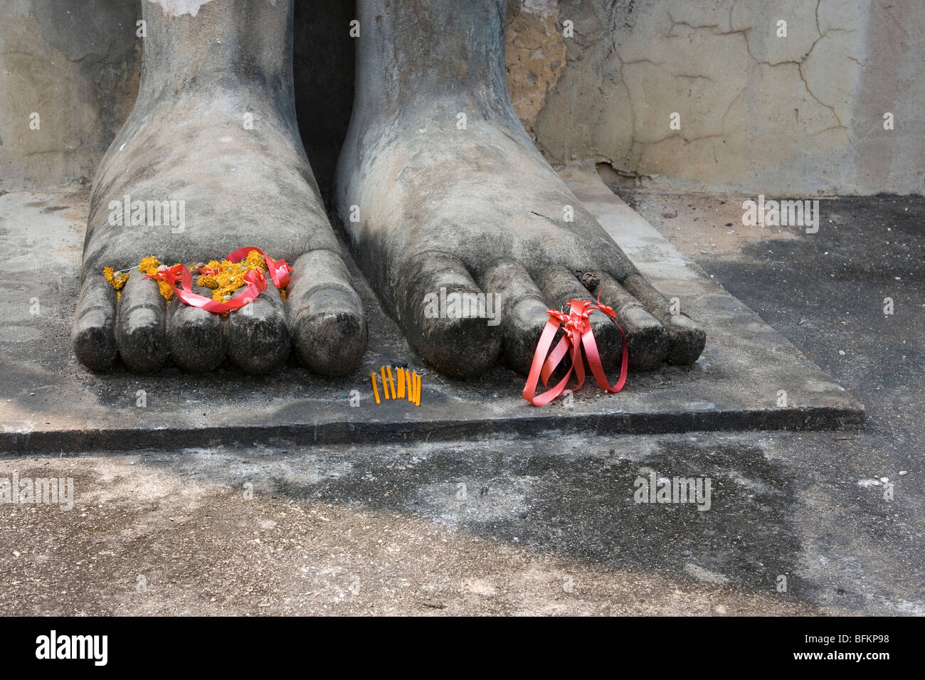 Pieds géant d'une statue de Bouddha Debout ornée de fleurs et de bougies en parc historique de Sukhothai, Thaïlande Banque D'Images