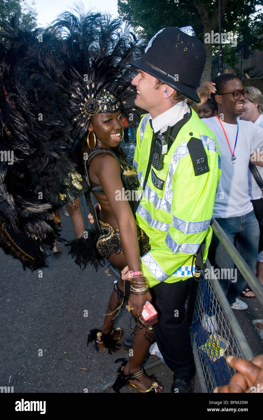 Fille du carnaval dans un costume de plumes noires danse avec un policier contre une clôture métallique au carnaval de Notting Hill 2009 Banque D'Images