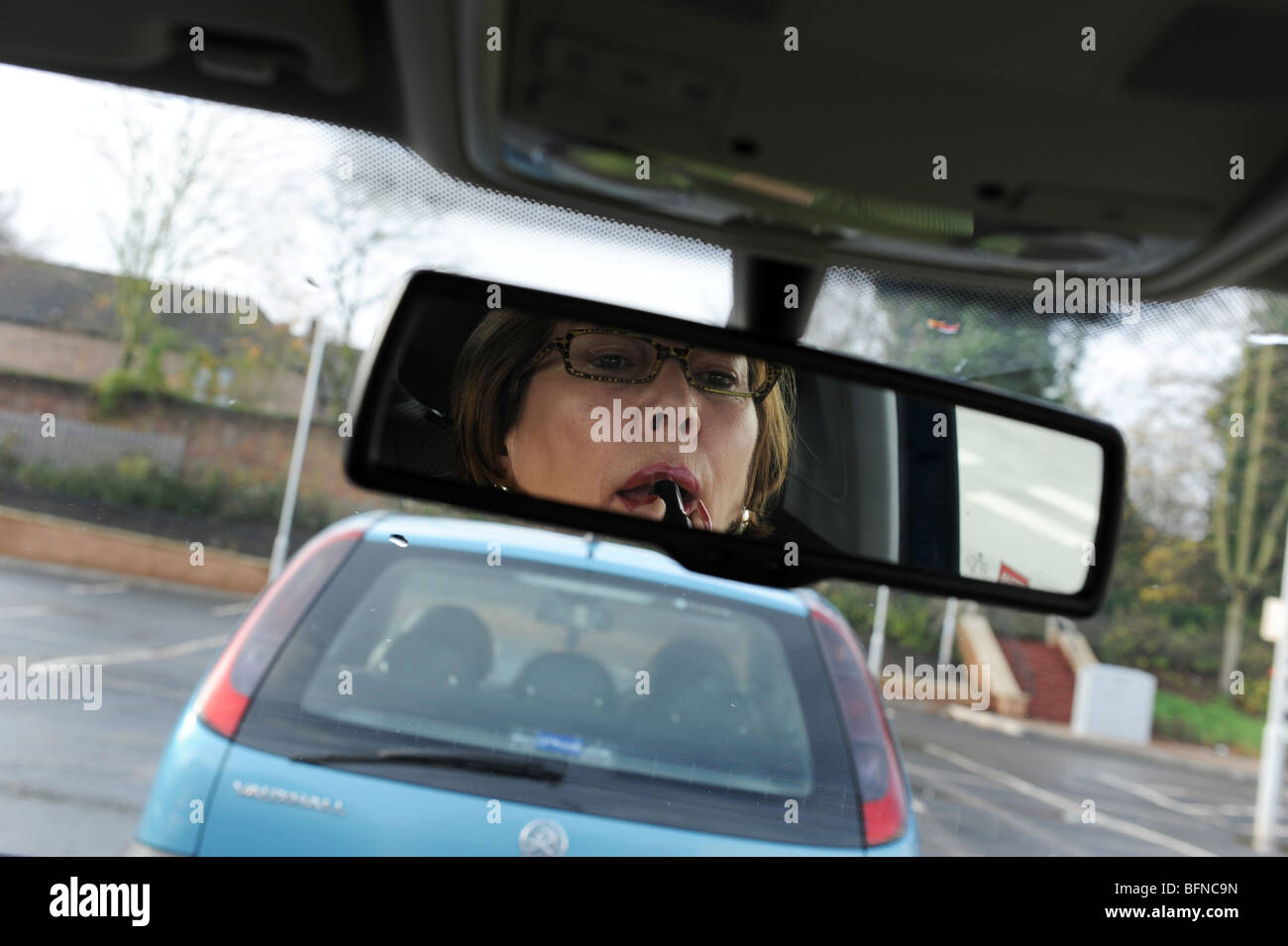 Female woman applying lipstick conducteur au volant de voiture uk Banque D'Images