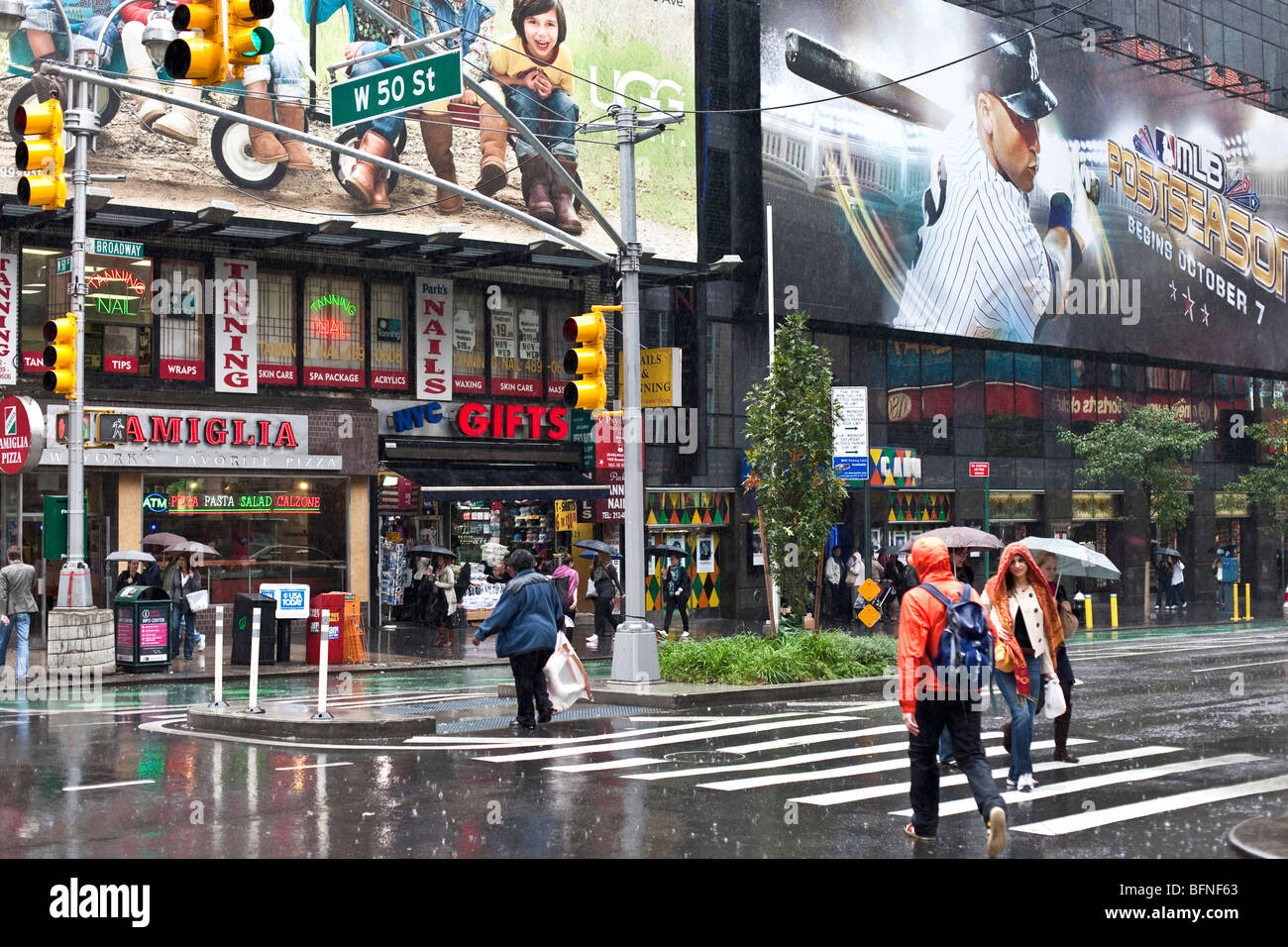 Peu de piétons dans des vêtements de pluie traversant Broadway à la 50e Rue Ouest un dimanche de fortes pluies diluviennes dans la région de New York City Banque D'Images
