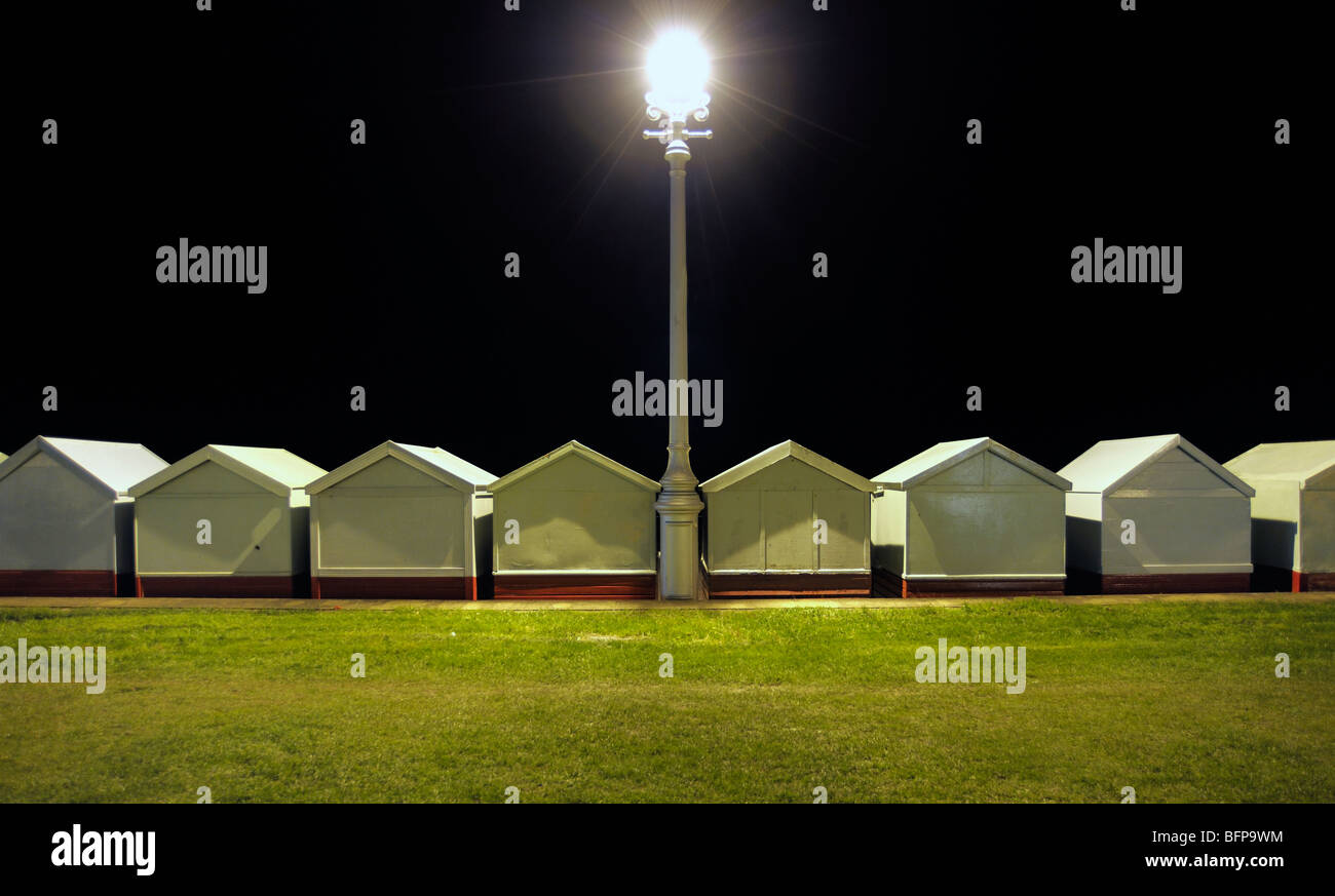 Une rangée de cabanes de plage éclairée par une vieille rue de lumière la nuit. Banque D'Images