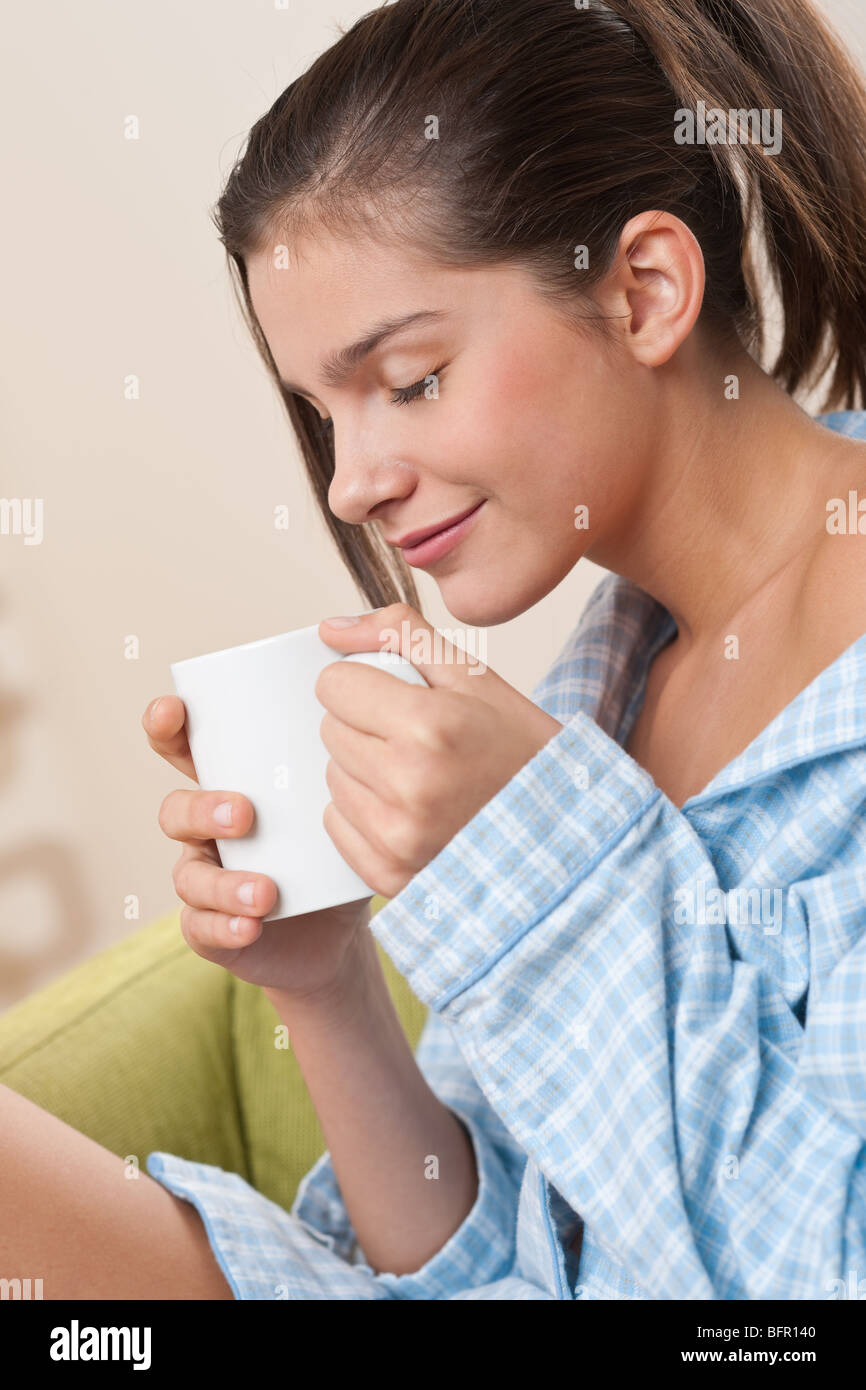 Les étudiants - une adolescente ayant tasse de café, wearing pajamas in modern living room Banque D'Images