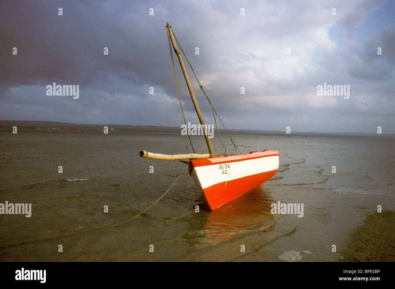 Dhow rouge et blanc sur la rive sous un ciel moody Banque D'Images