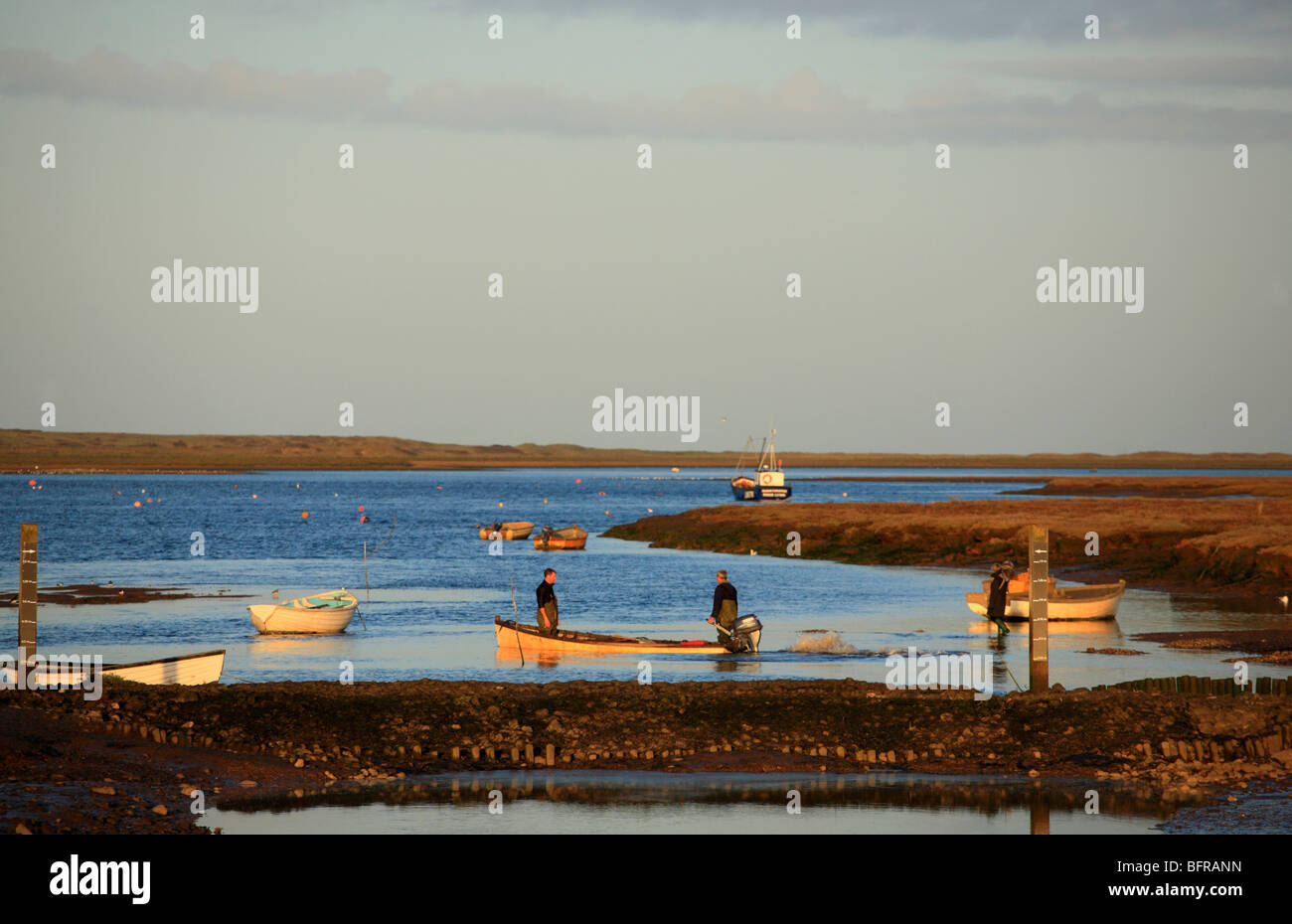 Deux pêcheurs de partir dans un petit bateau comme le soleil se couche à Brancaster Staithe sur la côte nord du comté de Norfolk. Banque D'Images