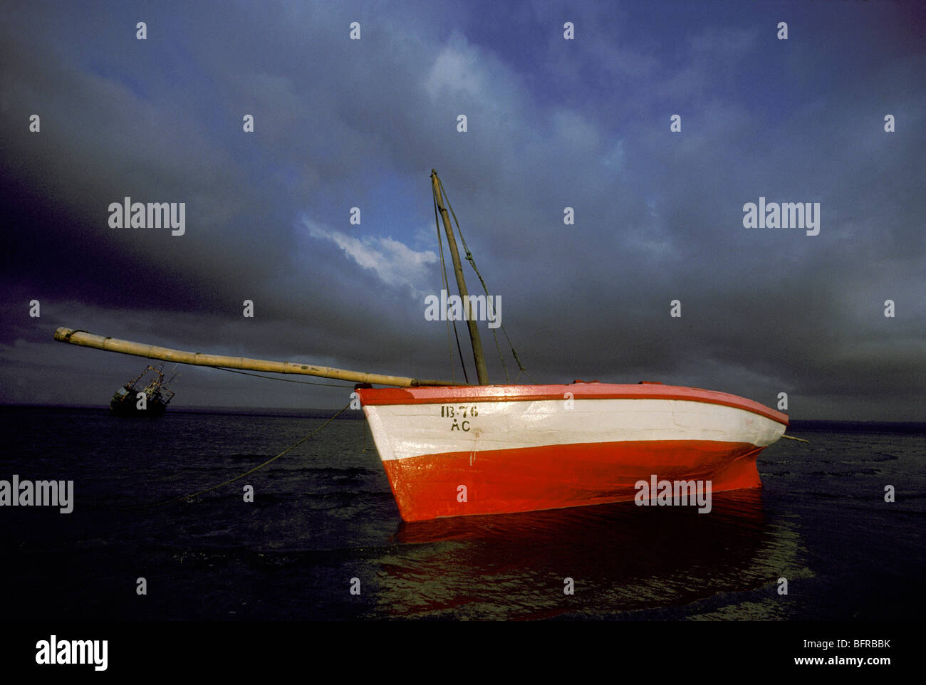 Dhow rouge et blanc sur la rive sous un ciel moody Banque D'Images