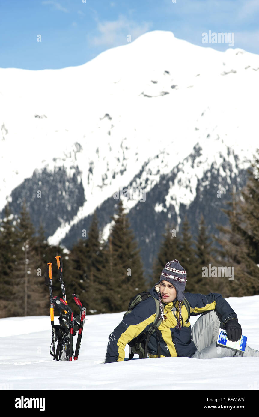 Jeune homme assis dans la neige avec matériel de randonnée Banque D'Images