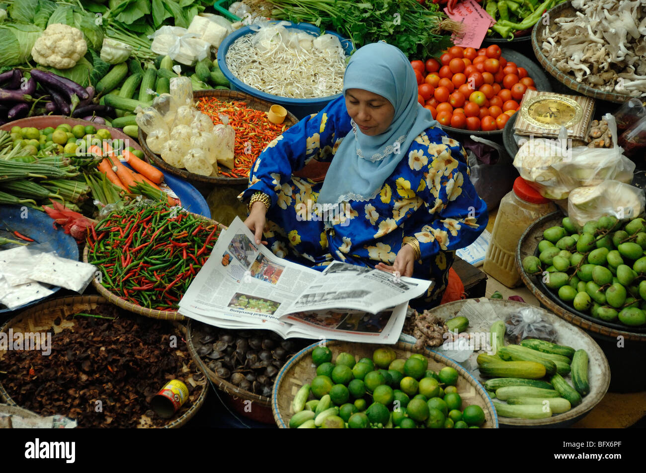 Le malais de Malaisie ou femme lisant un journal quotidien sur l'étal de légumes du marché, Marché Central, Kota Bahru, Malaisie Banque D'Images