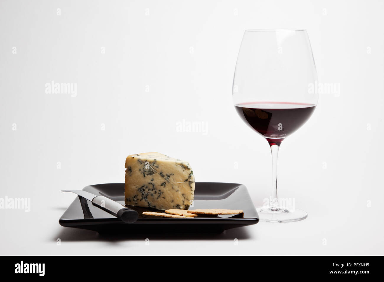 Coin de Stilton accompagné d'un verre de vin rouge et les craquelins sur une plaque noire avec couteau à fromage. Banque D'Images