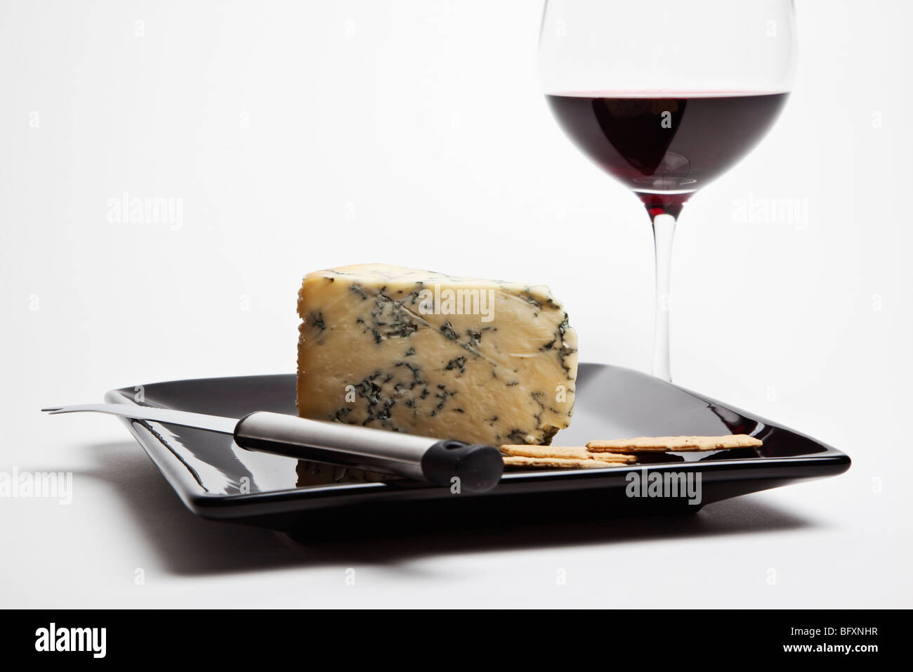 Coin de Stilton accompagné d'un verre de vin rouge et les craquelins sur une plaque noire avec couteau à fromage. Banque D'Images