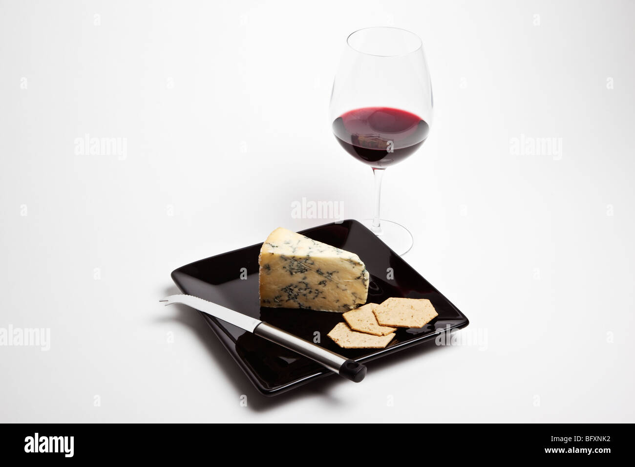 Coin de Stilton accompagné d'un verre de vin rouge et les craquelins sur une plaque noire avec couteau à fromage. Banque D'Images