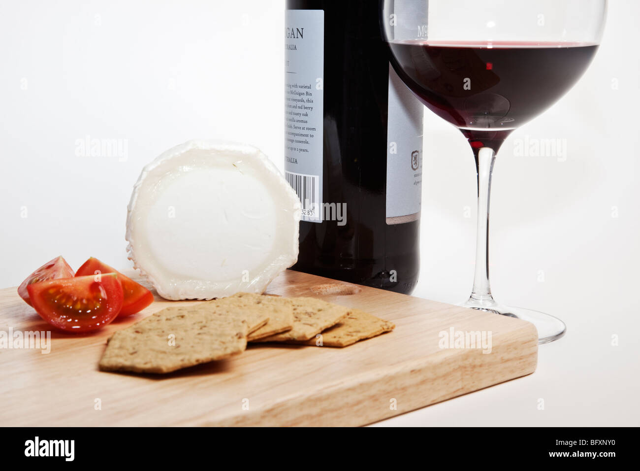 Avec fromage de chèvre et tomates craquelins sur un plateau à fromage en bois accompagné d'une bouteille et un verre de vin rouge. Banque D'Images