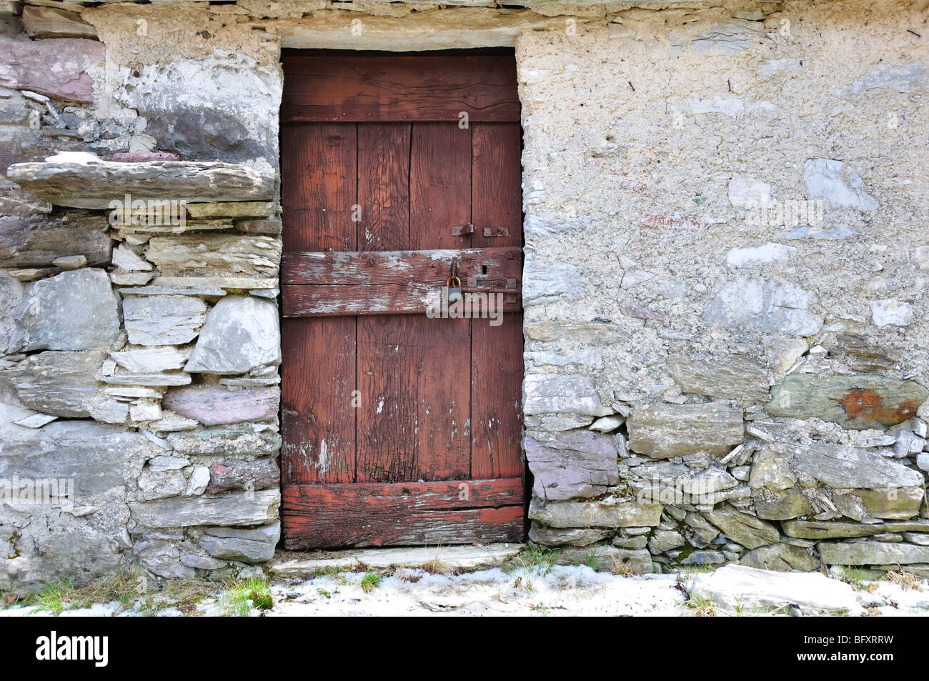 Vieille porte en bois dans un mur de pierre d'un ancien bâtiment d'un village de montagne abandonnés dans les Alpes italiennes Banque D'Images