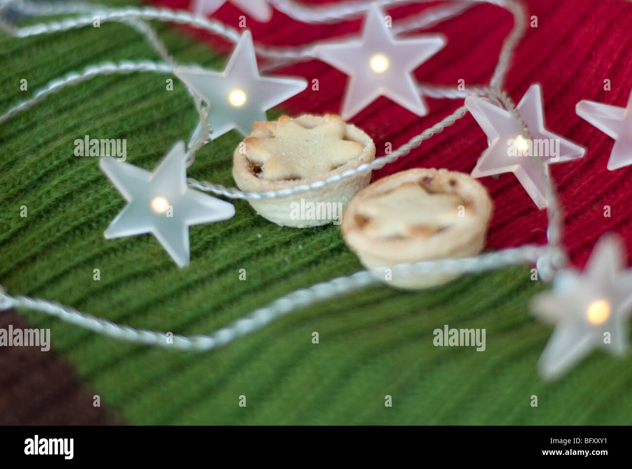 Petits pâtés de noël et star fairy lights-couché sur un vert, rouge et marron écharpe en laine à motifs Banque D'Images